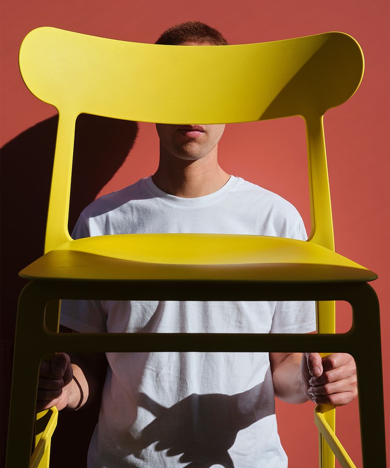 A yellow Lightly stacking chair held up in front of a red background.